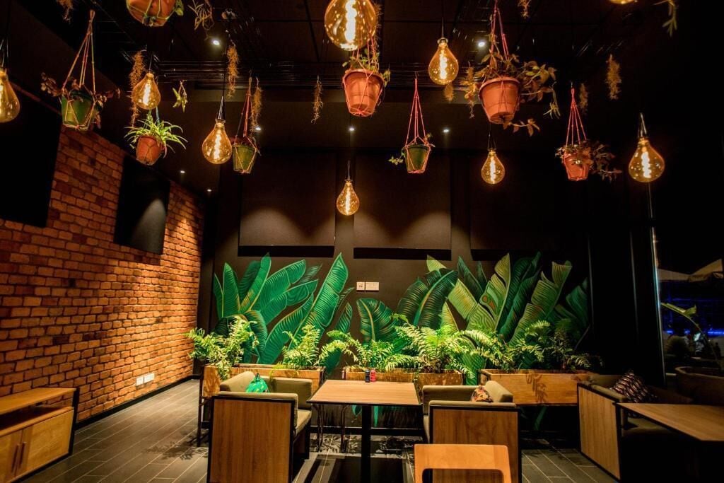 A restaurant interior with hanging light fixtures, brick walls, and a variety of potted plants.