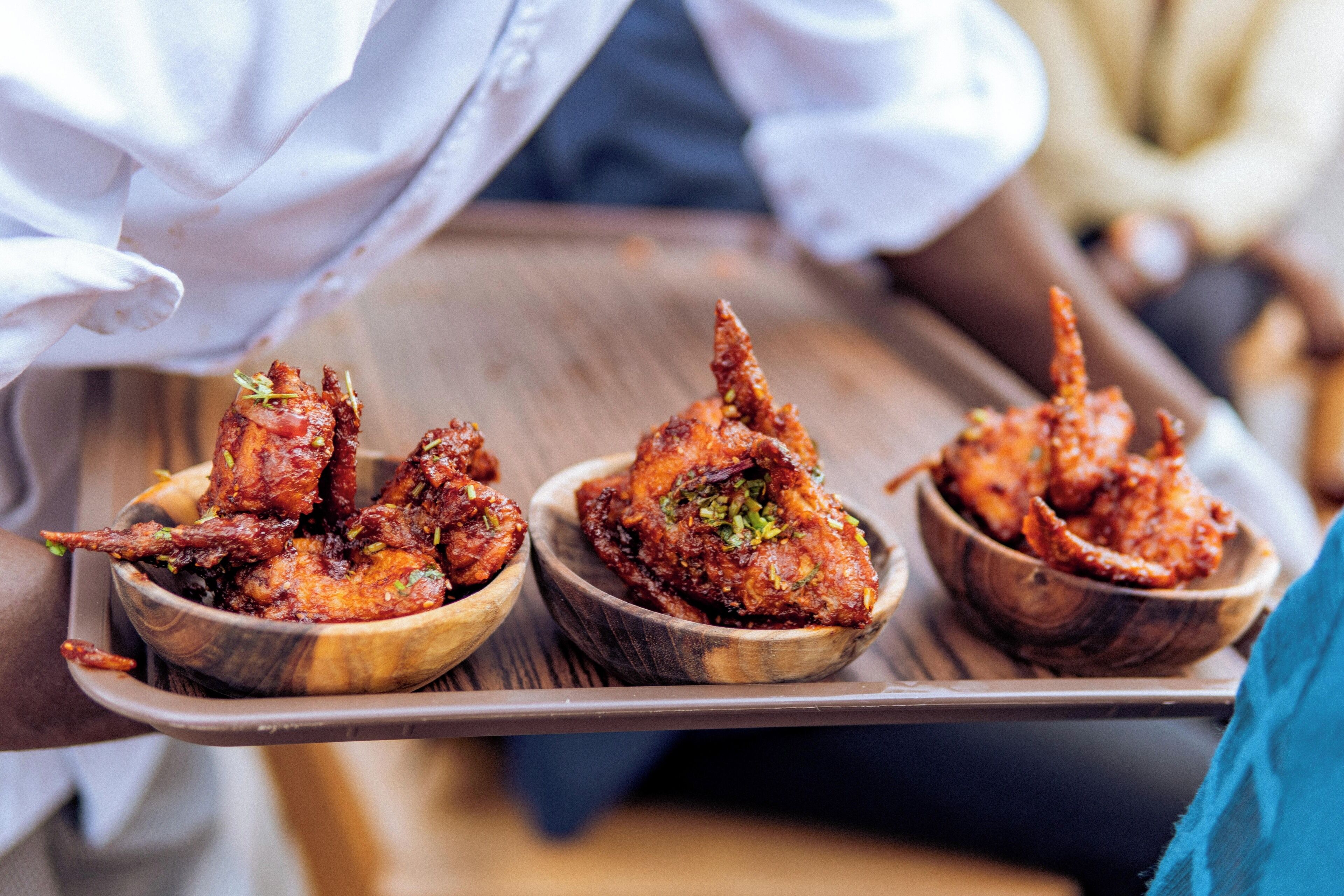 A tray with three wooden bowls containing fried chicken.