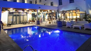 Een hotel met een zwembad, terras en een goed verlichte gevel.