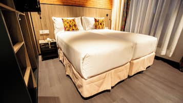 A double bed with a beige bed skirt, a wooden headboard, and a nightstand with a phone and a lamp.