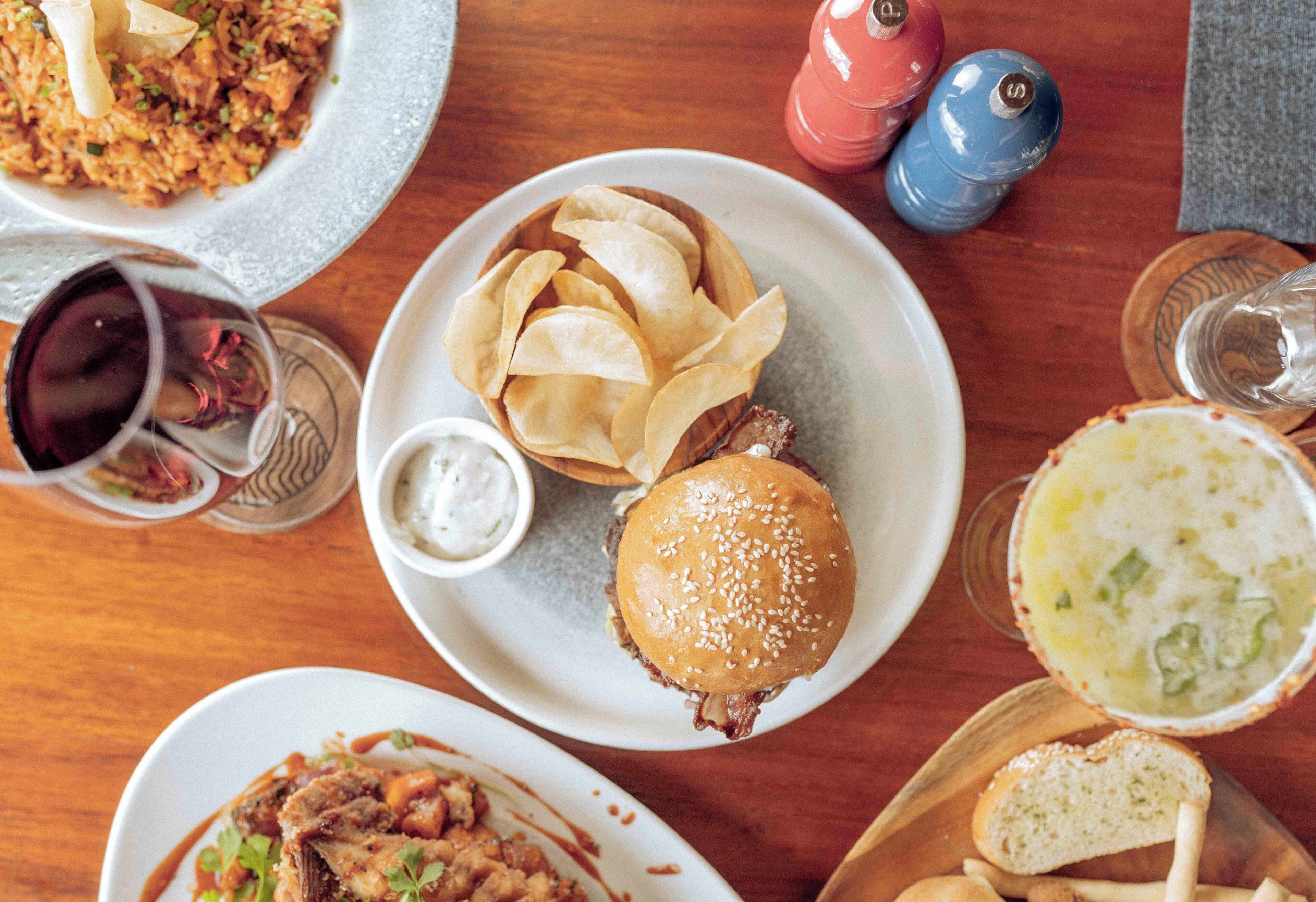A variety of dishes including a burger, chips, and soup on a wooden table.