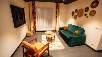 Una sala de estar con un sofá verde, un sillón de madera y una mesita redonda.