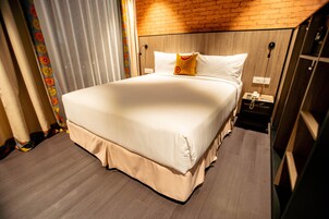 A hotel room with a large bed, a wooden headboard, a nightstand, and a power outlet.
