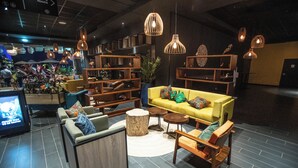 Een moderne zithoek met een gele bank, houten stoelen en een televisiescherm.