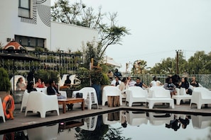 An outdoor seating area with white plastic chairs and tables, surrounded by greenery and a pool. - ONOMO Hotel Kampala (Kampala)