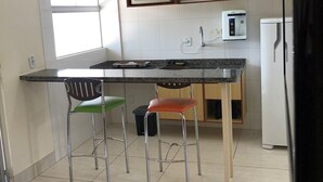 Una cucina compatta con isola centrale, due sgabelli da bar, un forno a microonde, una macchina da caffè e un frigorifero.