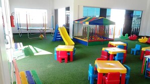 Un'area giochi con una piscina di palline, strutture per arrampicarsi e tavoli e sedie colorati.