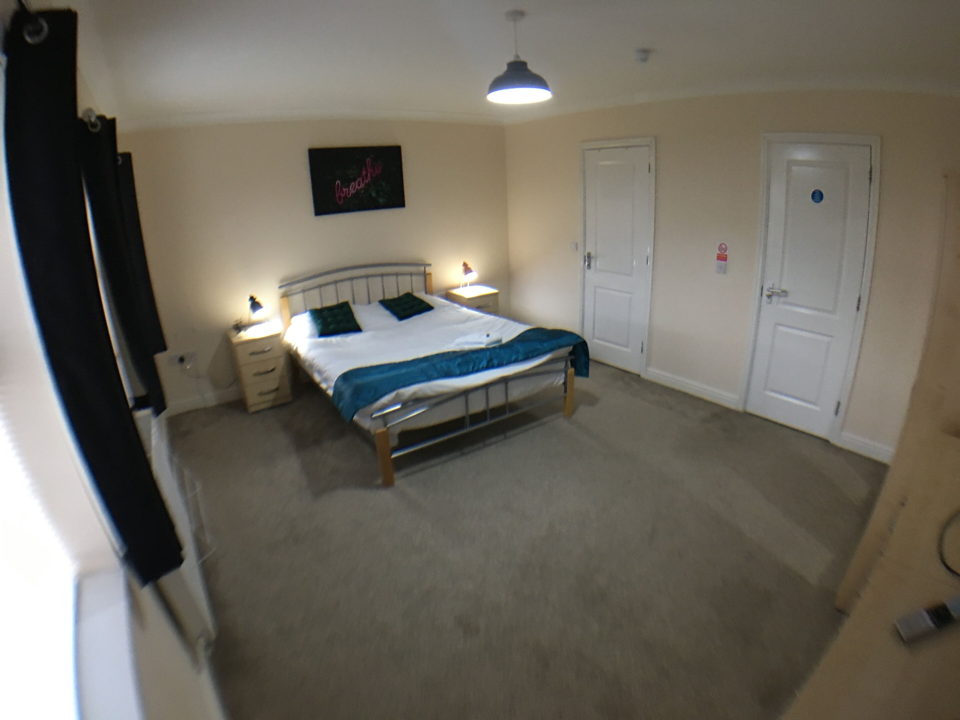 Une chambre à coucher avec un lit, des tables de chevet, une lampe suspendue et une porte.