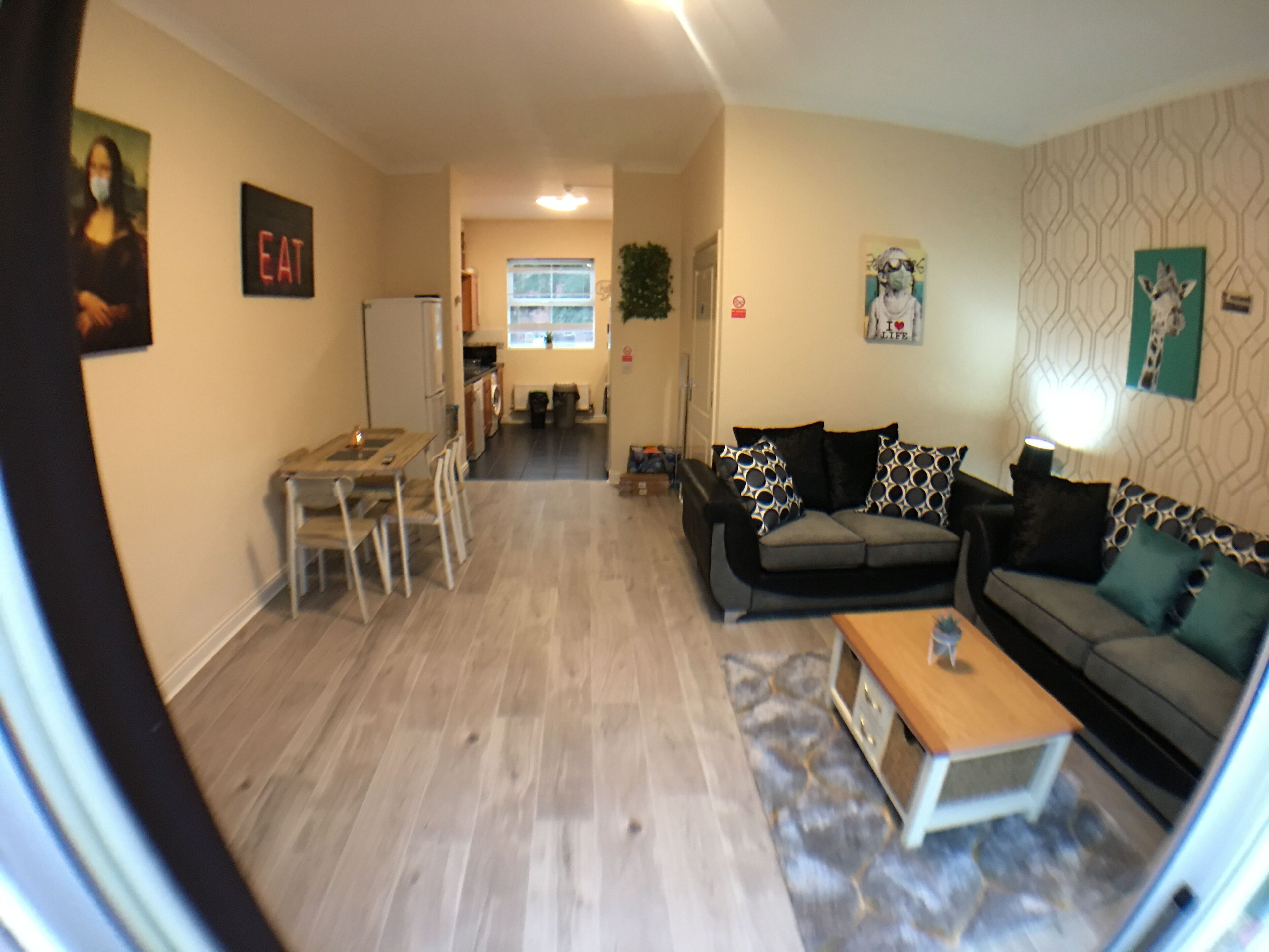 A living room with a sofa, coffee table, and dining area. There is a kitchen in the background.