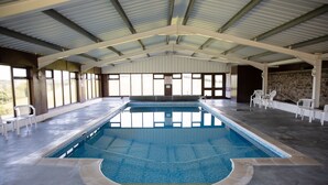 An indoor swimming pool with a tiled floor, a diving board, and white chairs around the perimeter. - Barn Conversion With Indoor Swimming Pool In Stunning Rural Location Near Ocean (Bude)