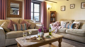 A cozy living room with two sofas, a coffee table with snacks and drinks, a bookshelf, and a window with curtains. - Barn Conversion With Indoor Swimming Pool In Stunning Rural Location Near Ocean (Bude)