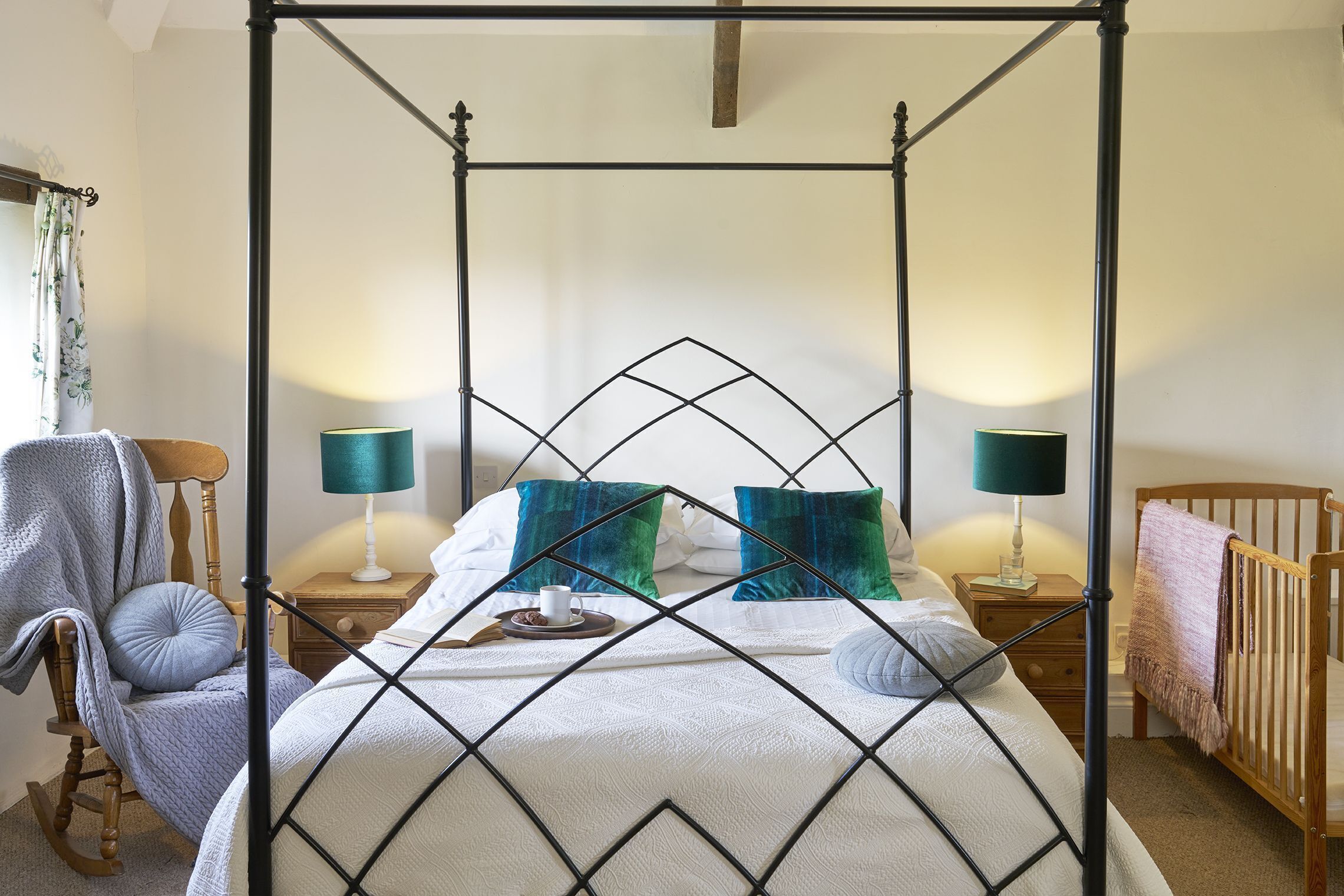 A four-poster bed with a white quilt, two teal lamps, and a wooden rocking chair.