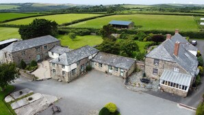 A stone building with a large open courtyard, surrounded by lush green fields and a few trees. - Barn Conversion With Indoor Swimming Pool In Stunning Rural Location Near Ocean (Bude)
