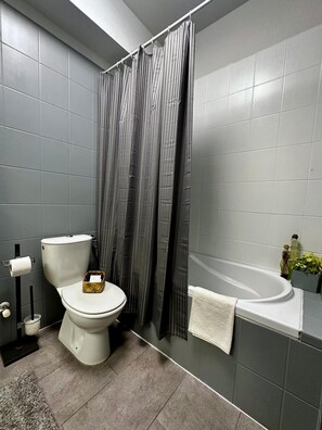 Ein Badezimmer mit Toilette, Duschvorhang, Badewanne und Handtuchhalter.