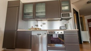 Cocina compacta con electrodomésticos de acero inoxidable, incluyendo lavavajillas, horno y microondas.