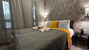 Ein modernes Hotelzimmer mit einem Kopfteil im geometrischen Muster, einem großen Bett mit einer Bettdecke, einem Nachttisch mit einer Lampe und transparenten Vorhängen.