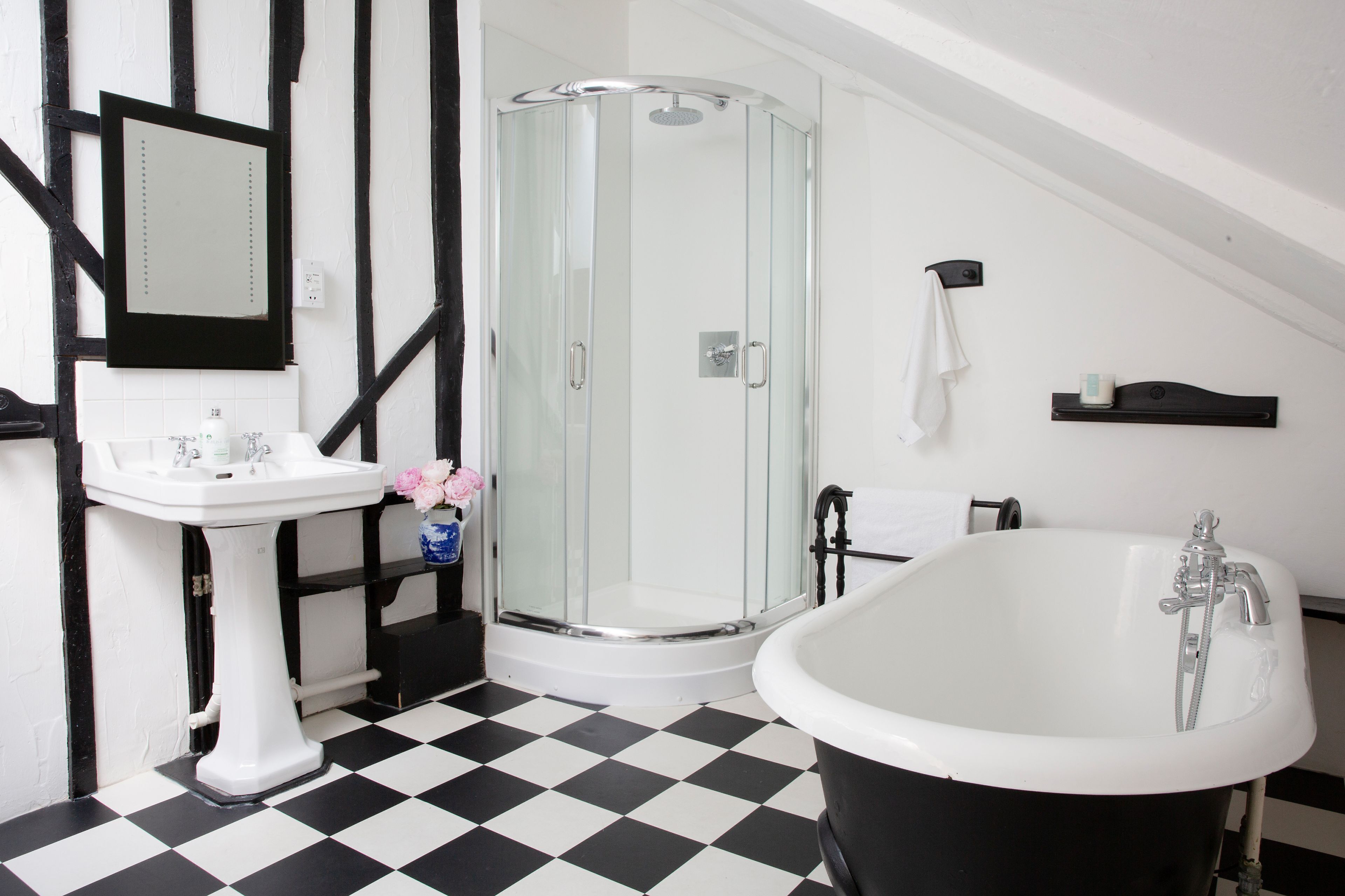 A bathroom with a black and white checkered floor, a white sink, a glass shower enclosure, and a freestanding bathtub.