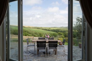 Un patio con una mesa y sillas de piedra, un jarrón con flores y vistas a colinas verdes.