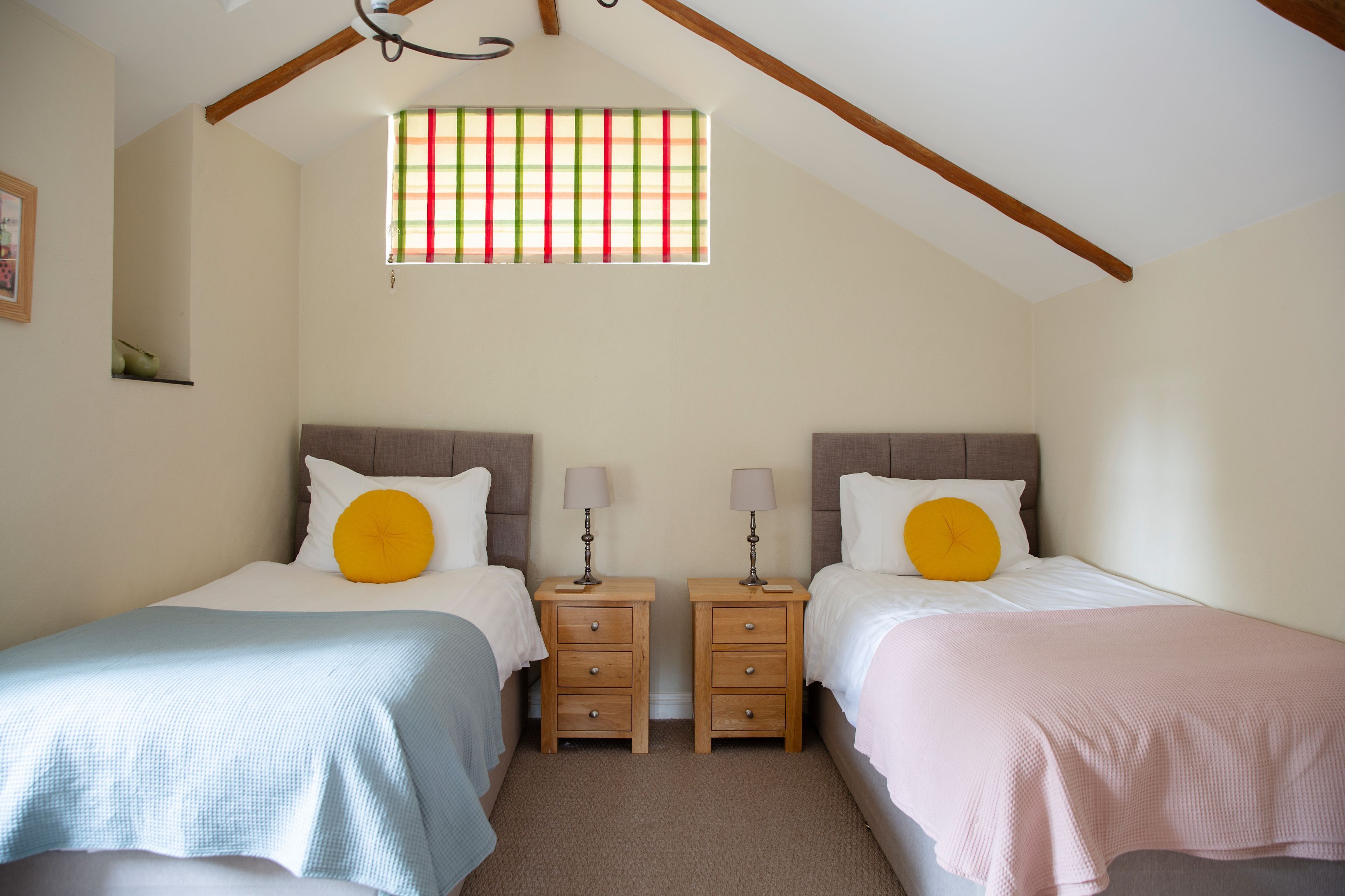 Quarto com duas camas, mesinhas de cabeceira de madeira e uma janela com persiana listrada.