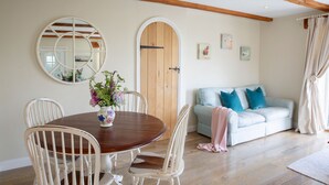 A dining area with a wooden table and white chairs, a round mirror, and a wooden door. - Luxury Cottage With Indoor Swimming Pool In Stunning Rural Location Near Ocean (Bude)