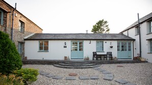 En vit byggnad med en blå dörr och fönster, en stentrappa som leder till entrén och en grusbelagd innergård.