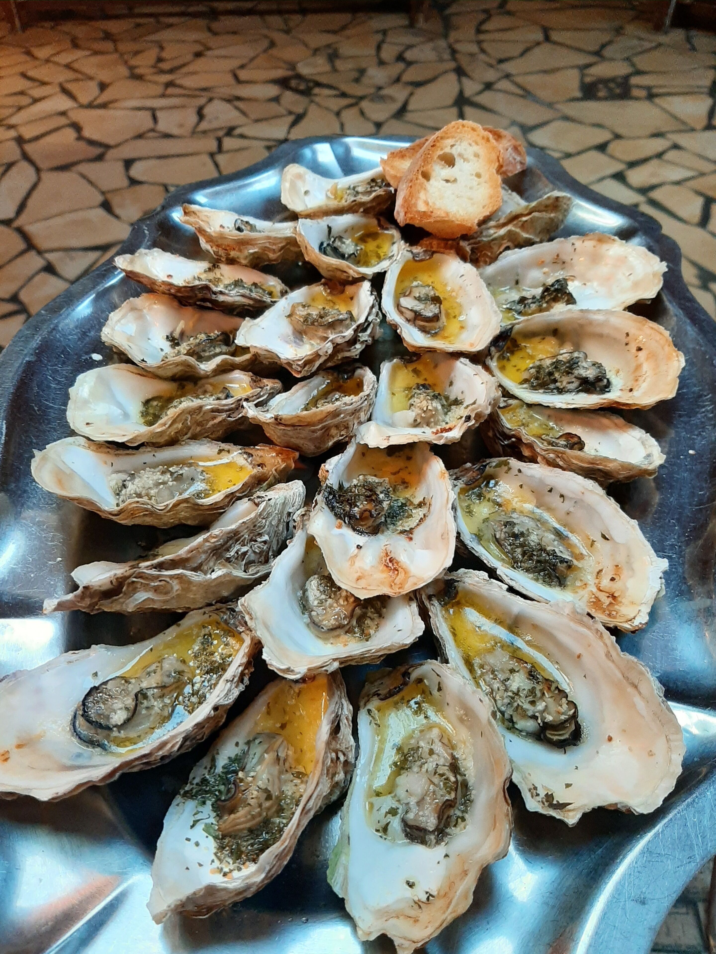 A plate of oysters with a slice of bread on a metal tray.