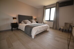 A modern bedroom with a large bed, two bedside tables with lamps, a chair, and a window with curtains. - Villa with a pool in Maussane-les-Alpilles, with an incredible view of the valley (Maussane-les-Alpilles)
