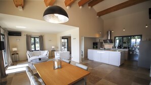 A spacious living area with a wooden dining table, a sofa, and a kitchen in the background. - Villa with pool in Maussane les Alpilles, incredible view of the valley (Maussane-les-Alpilles)