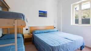 Une chambre avec un lit superposé, un lit simple, une table de chevet, une commode et une fenêtre donnant sur un paysage verdoyant.