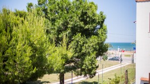 Une vue sur la côte, avec un grand pin, un sentier menant à une plage et un bâtiment blanc surmonté d’un toit rouge.
