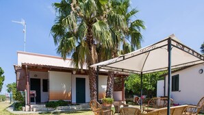 Une maison dotée d’un patio couvert, de meubles en osier et d’un palmier.
