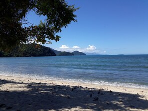 Ein Strand mit klarem Wasser, einem sandigen Ufer und fernen Bergen.