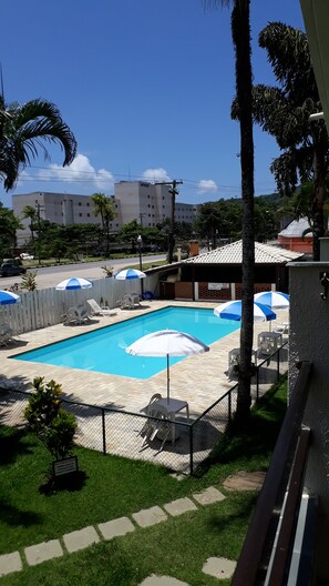 A swimming pool with lounge chairs and umbrellas, surrounded by a fence and palm trees.