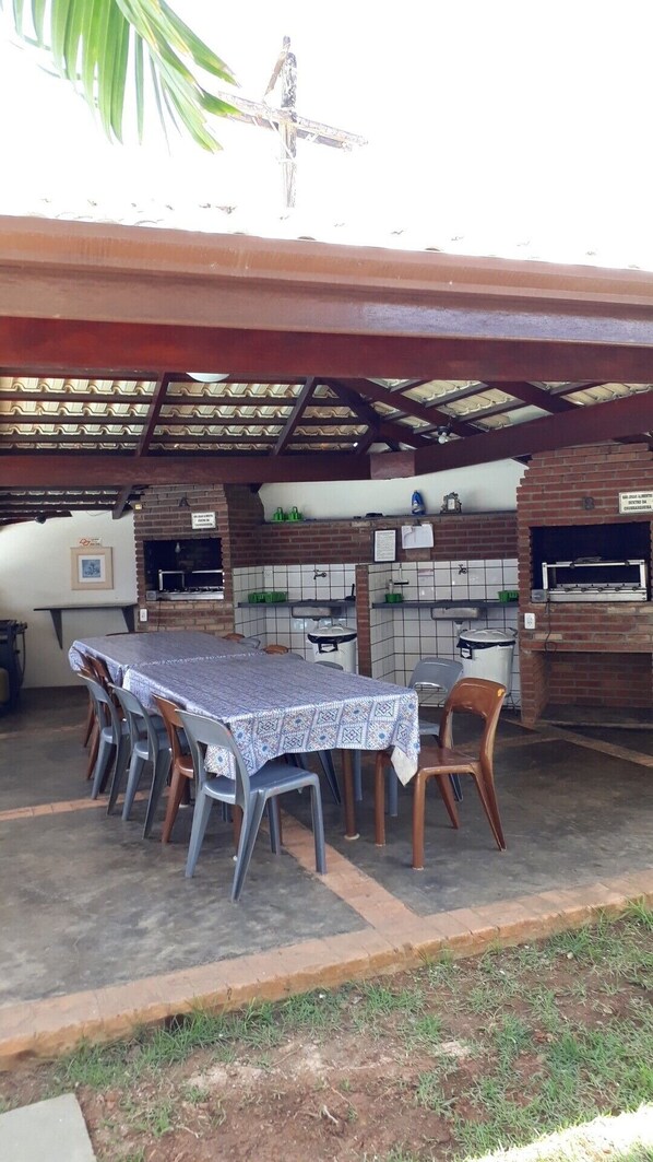 Eine Terrasse im Freien mit einem Ziegelbackofen, einem Tisch mit Stühlen und einem überdachten Bereich mit Metallveranda.