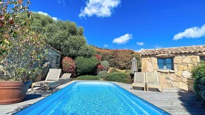 Ein Pool mit Liegestühlen, umgeben von üppiger Vegetation und einem Gebäude mit einem Ziegeldach.