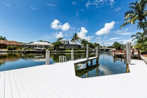 A waterfront property with a dock, a pool, and a house with a covered patio.