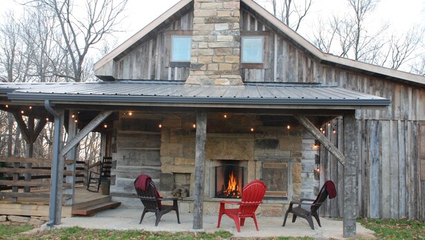 A rustic cabin with a stone fireplace, two red Adirondack chairs, and a covered porch area.