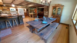 A rustic kitchen with wooden floors, a large wooden dining table set for four, and a chandelier.