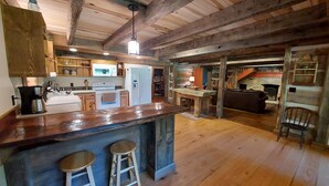 A rustic kitchen with wooden beams, a large island with stools, and a dining area with a fireplace.