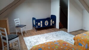 Una camera da letto con soffitto spiovente, un letto blu con pannelli decorativi, una sedia bianca e un tappeto colorato.