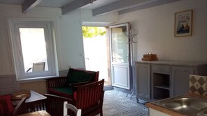 Zona pranzo con tavolo e sedie in legno, una poltrona con cuscino verde, angolo cottura con lavello e pensili, e pavimento decorato.
