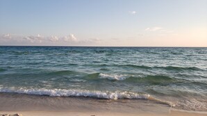 A beach with waves gently lapping onto the shore, a clear sky, and a distant horizon.