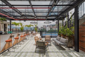 Un bar situé sur le toit, avec des places assises, une vue sur la piscine et un panorama sur la ville en arrière-plan.