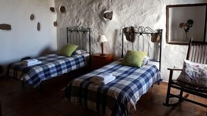 Een kamer met twee bedden, elk met een geruit beddekleed en een kussen. Daartussen bevindt zich een nachtkastje met een lamp. De muren hebben een structuurafwerking met decoratieve details.