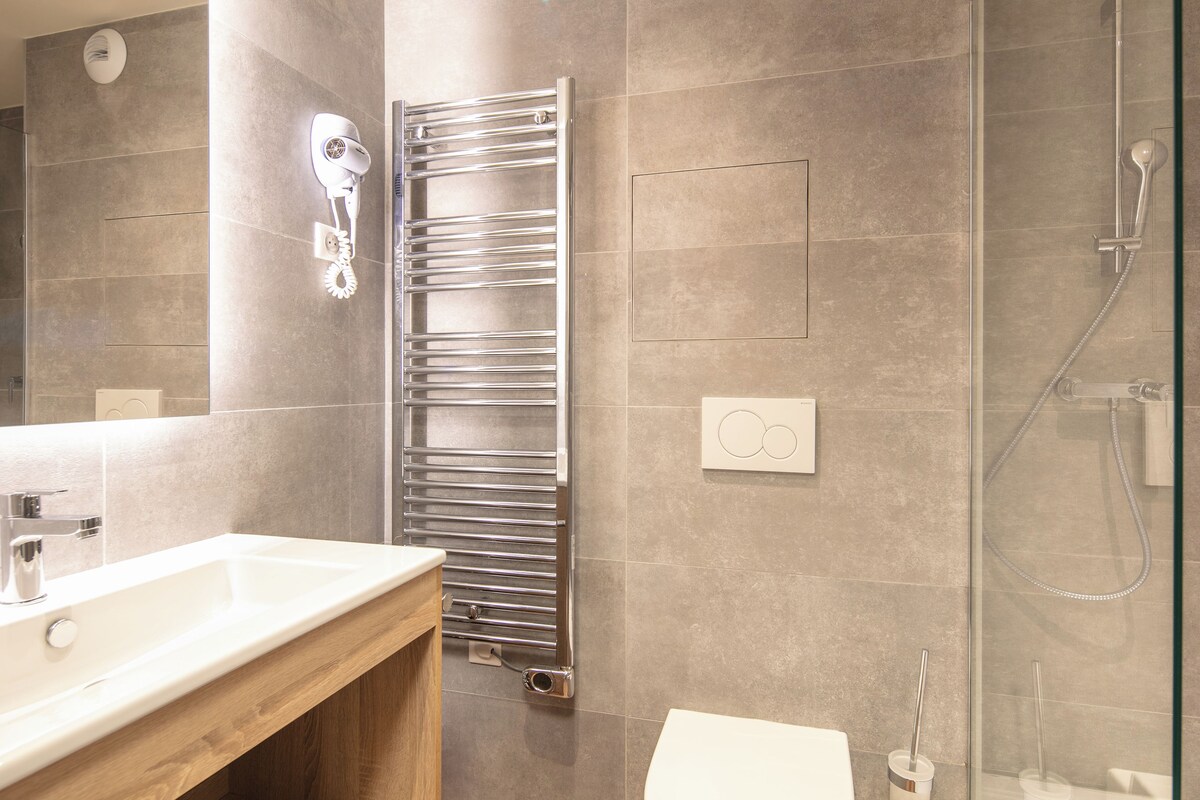 A modern bathroom with a wooden vanity, a chrome towel rack, a toilet, and a glass shower enclosure.