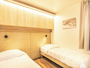 Un dormitorio con dos camas individuales, cabecero de madera, lámparas de noche y un cuadro colgado en la pared.