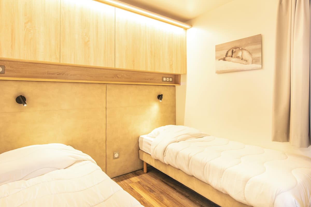 A bedroom with two single beds, wooden headboard, bedside lamps, and a wall-mounted painting.