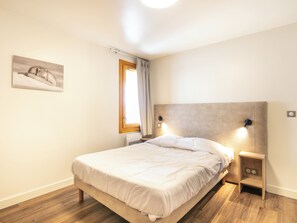 A bedroom with a bed, a nightstand, a wall-mounted lamp, a window with curtains, and a painting on the wall. - Residence La Duit - Vacanceole (La Léchère)
