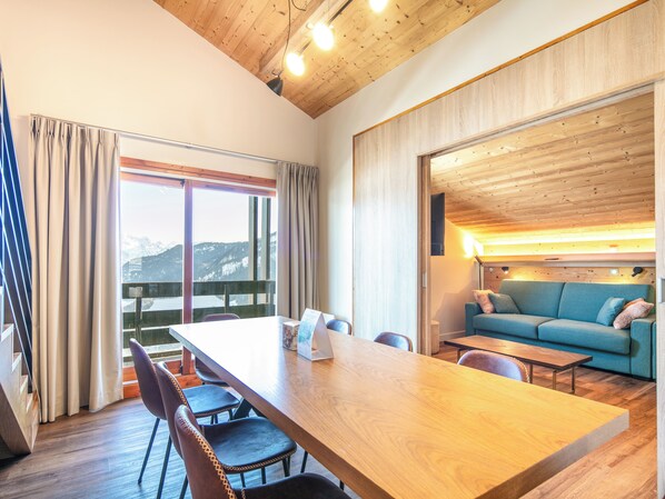 A modern room with a wooden ceiling, a large table with chairs, a sofa, and a view of snow-capped mountains through large windows. - Residence La Duit - Vacanceole (La Léchère)