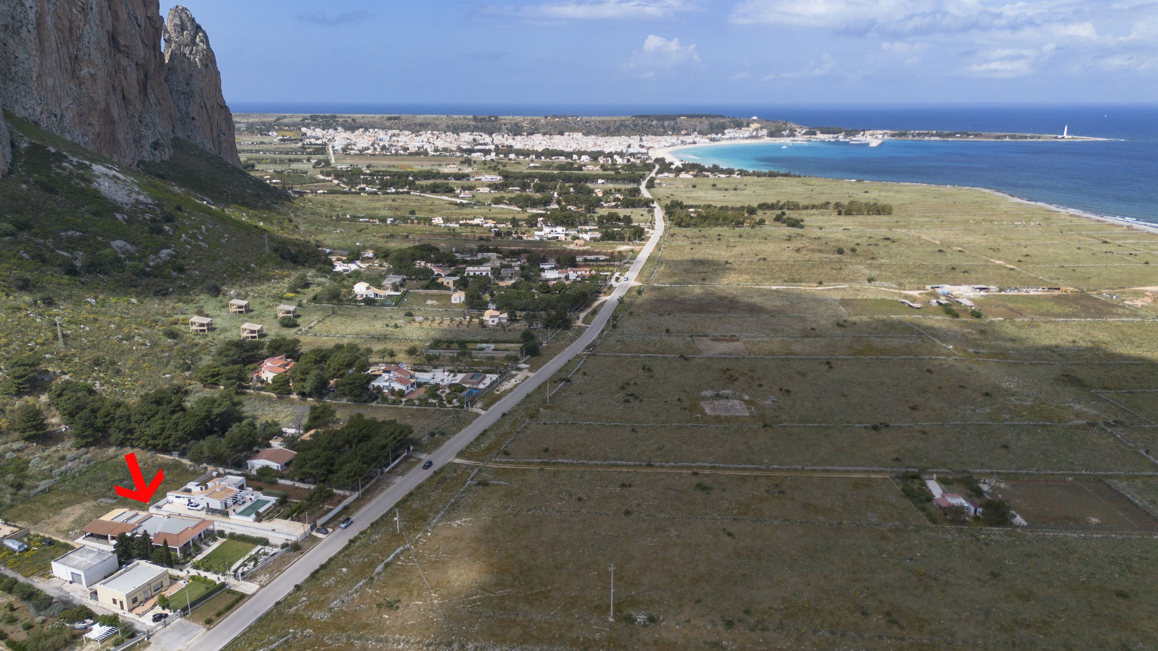 Luftaufnahme einer Küstenstadt mit einer markanten Klippe, einem Strand und einer Straße, die an der Stadt entlangführt.